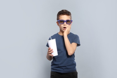 Photo of Emotional boy with 3D glasses and beverage during cinema show on grey background