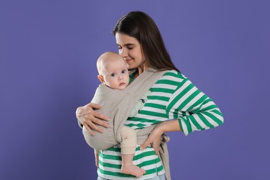 Photo of Mother holding her child in sling (baby carrier) on purple background