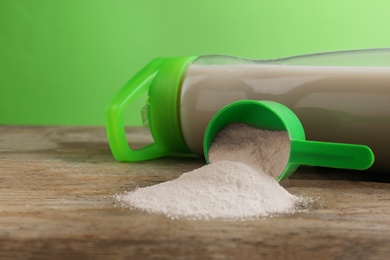 Measuring scoop of protein powder and bottle with shake on wooden table. Space for text