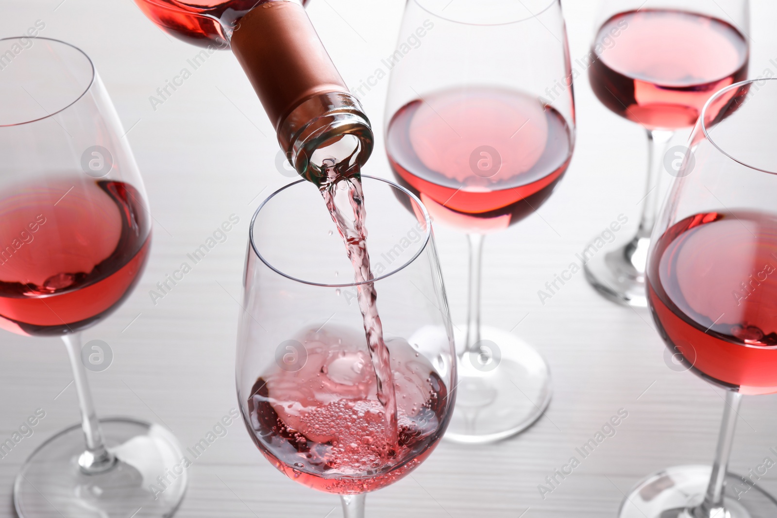 Photo of Pouring rose wine from bottle into glasses on wooden table, closeup