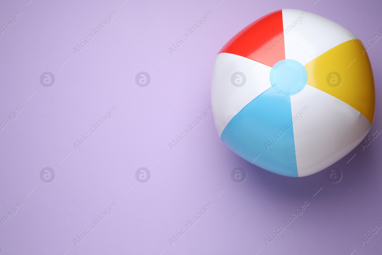 Photo of Colorful beach ball on violet background, top view. Space for text