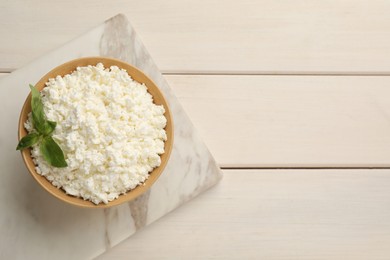 Photo of Delicious fresh cottage cheese with basil on white wooden table, top view. Space for text