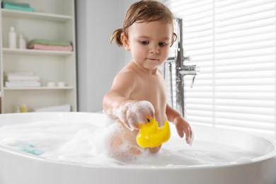 Photo of Cute little girl with rubber duck in bathtub at home