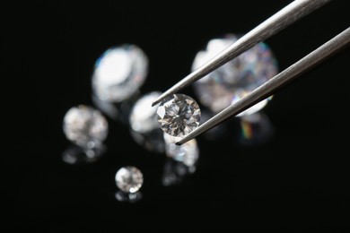 Photo of Tweezers with beautiful shiny diamond against black background, closeup