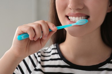 Photo of Woman brushing her teeth with plastic toothbrush indoors, closeup