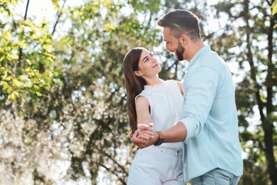 Lovely young couple dancing together in park on sunny day