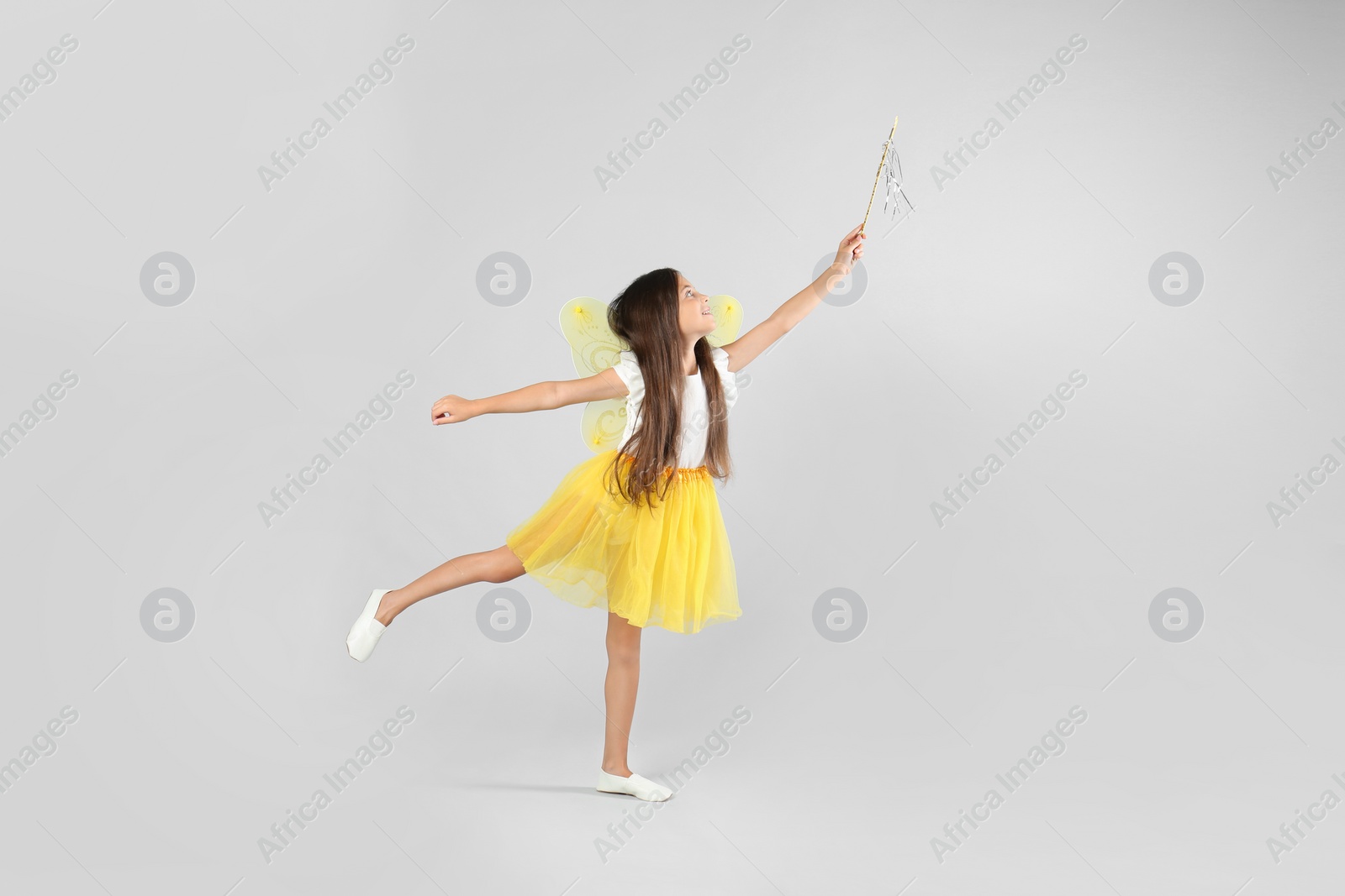 Photo of Cute little girl in fairy costume with yellow wings and magic wand on light background