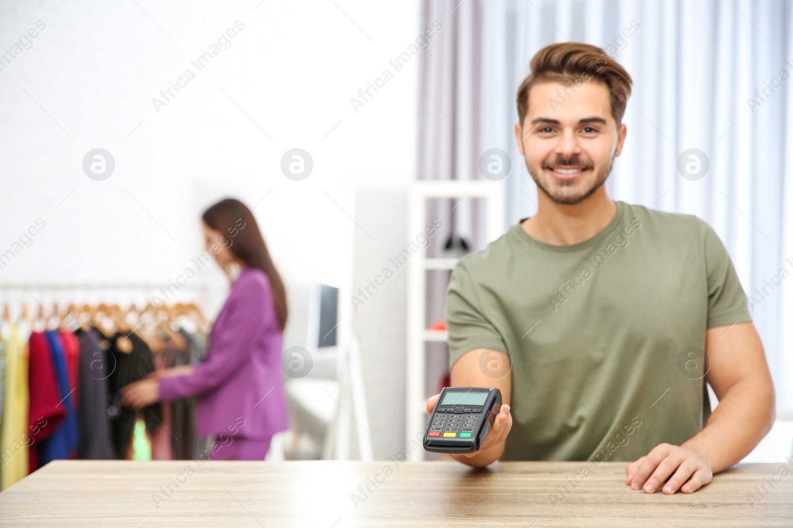 Photo of Male shop assistant with payment terminal at counter. Space for text