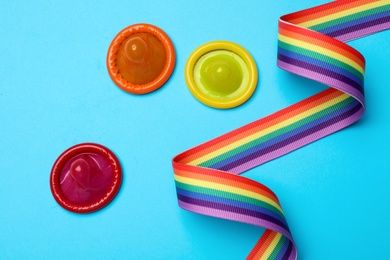 Colorful condoms and rainbow ribbon on light blue background, flat lay. LGBT concept