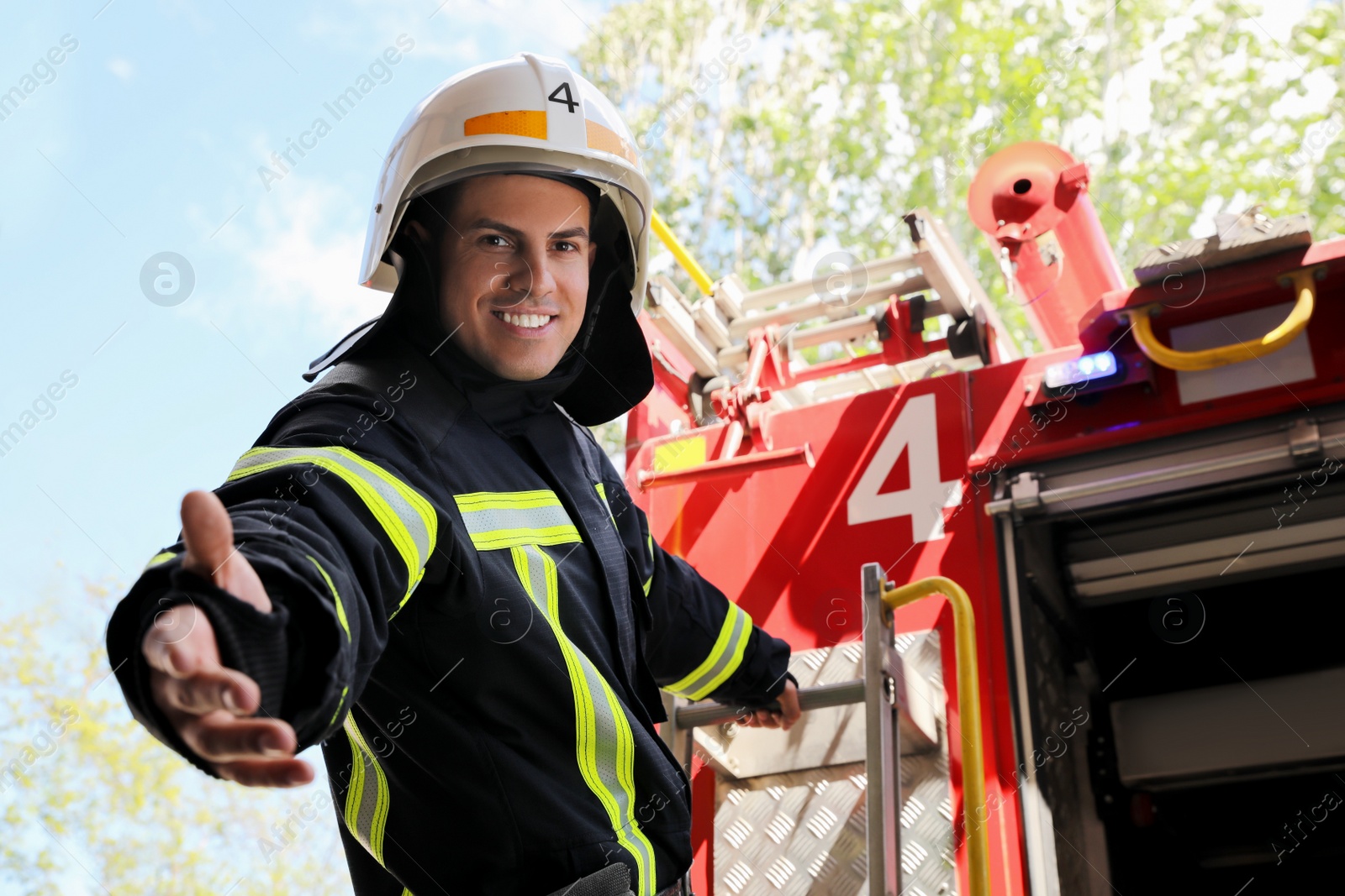 Photo of Firefighter in uniform and helmet offering hand near fire truck outdoors