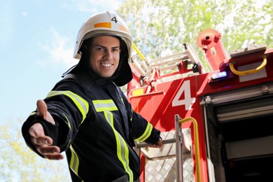 Firefighter in uniform and helmet offering hand near fire truck outdoors