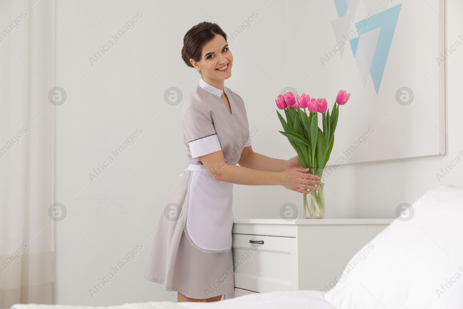 Photo of Young maid with flowers in hotel room