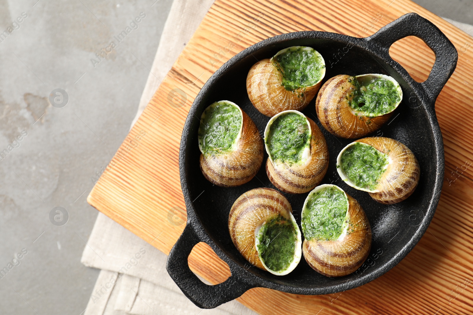 Photo of Delicious cooked snails in baking dish on grey table, top view