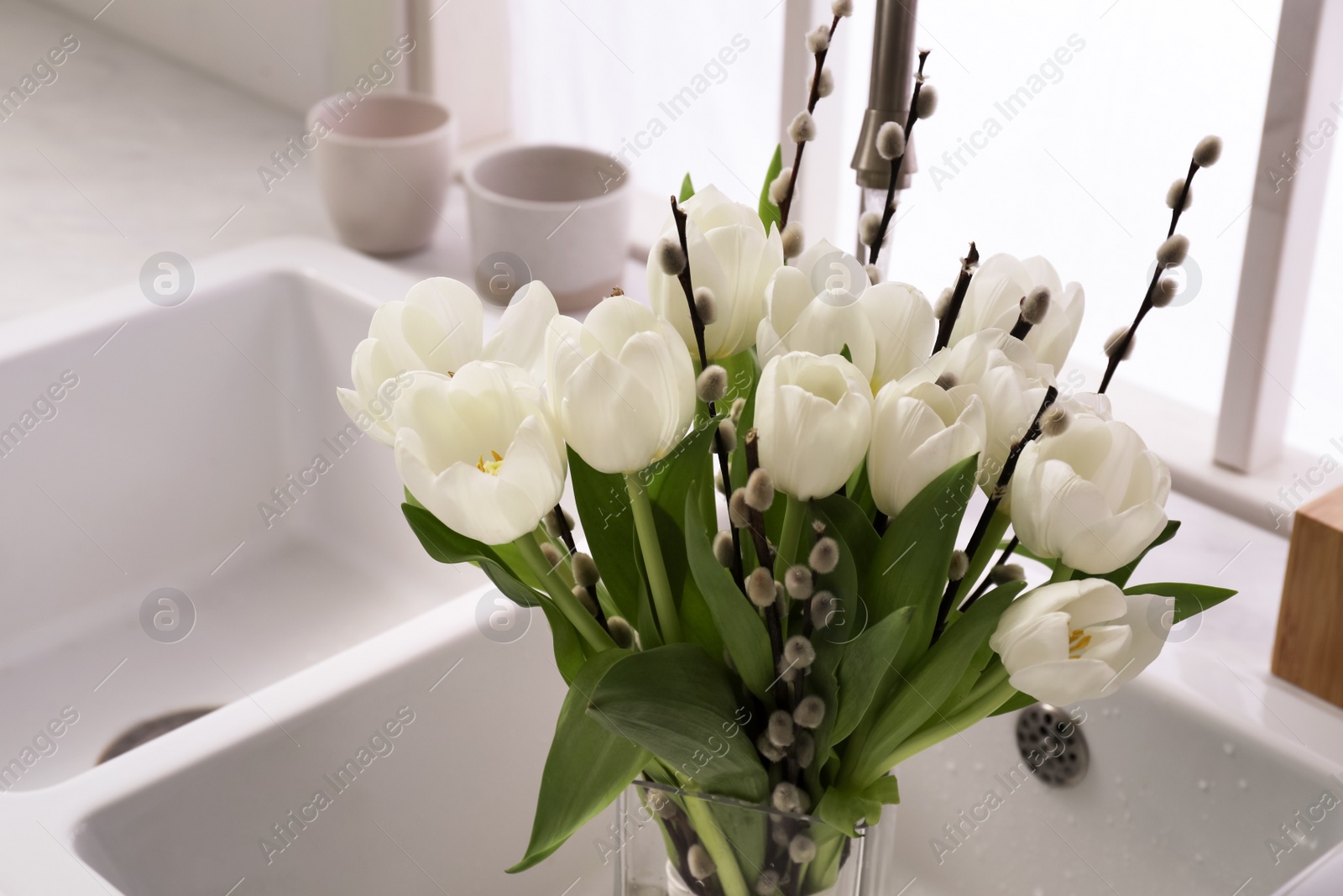 Photo of Beautiful bouquet of willow branches and tulips in kitchen sink