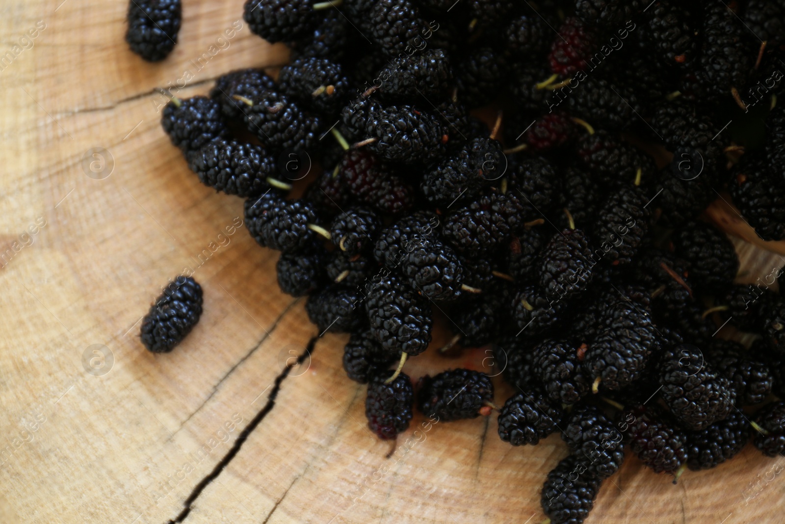 Photo of Heap of delicious ripe black mulberries on wood stump, top view