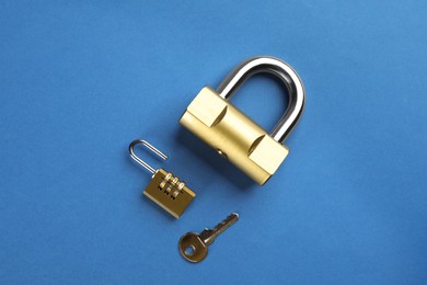 Photo of Modern padlocks with key on blue background, flat lay