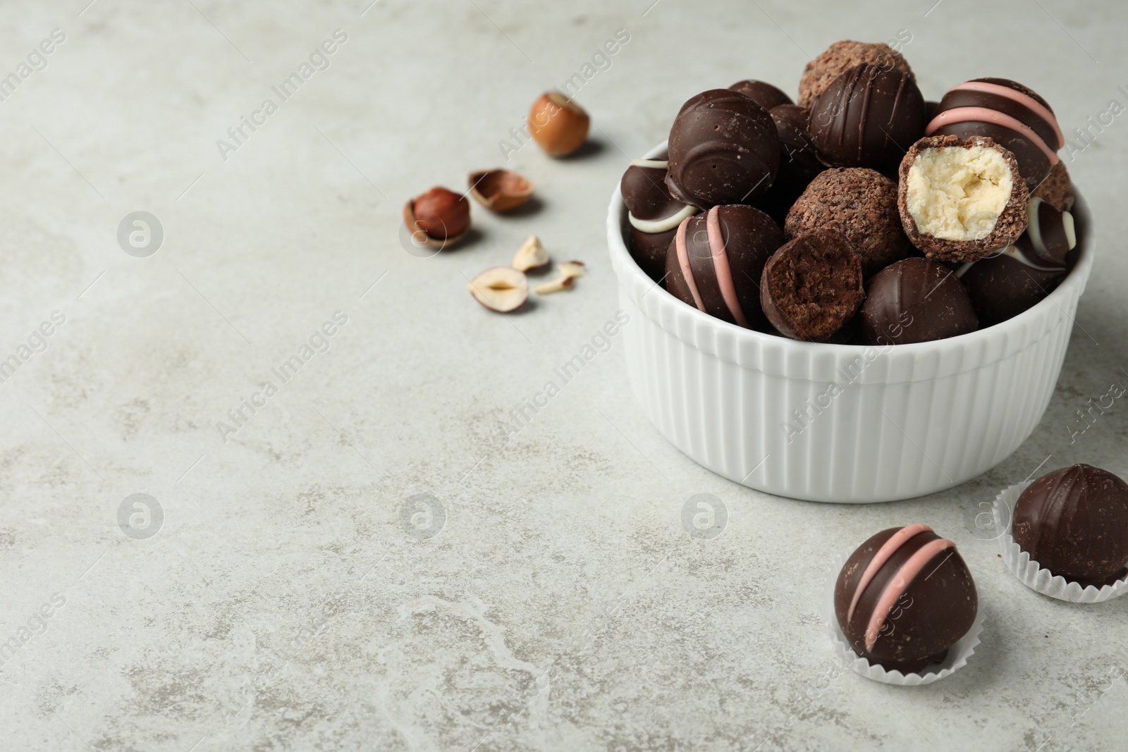 Photo of Different delicious chocolate truffles in bowl on light grey table. Space for text