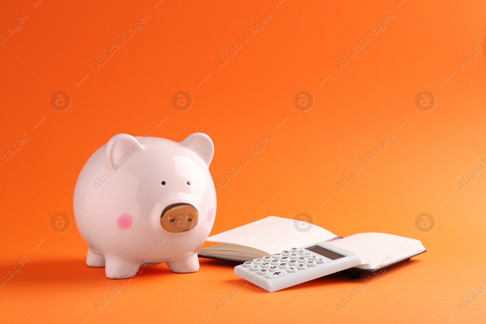 Photo of Financial savings. Piggy bank, notebook and calculator on orange background