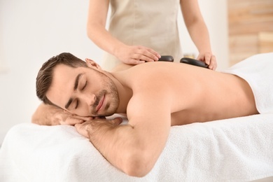 Photo of Handsome man receiving hot stone massage in spa salon