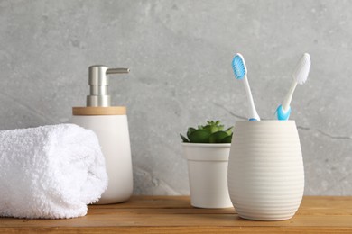Photo of Plastic toothbrushes in holder, towel, potted plant and cosmetic product on wooden table