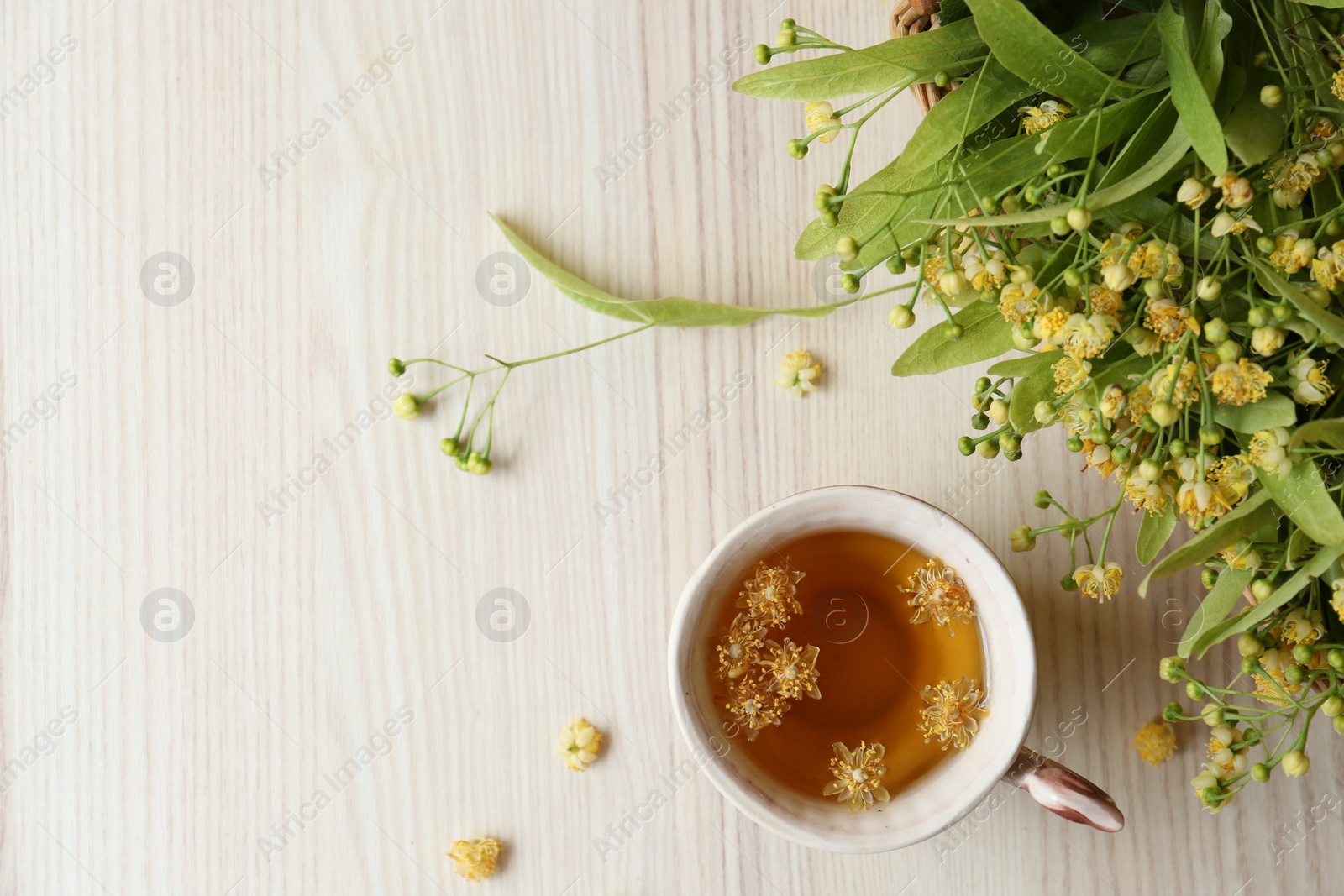 Photo of Cup of aromatic tea with linden blossoms on white wooden table, flat lay. Space for text