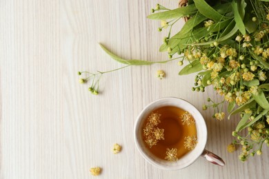 Photo of Cup of aromatic tea with linden blossoms on white wooden table, flat lay. Space for text
