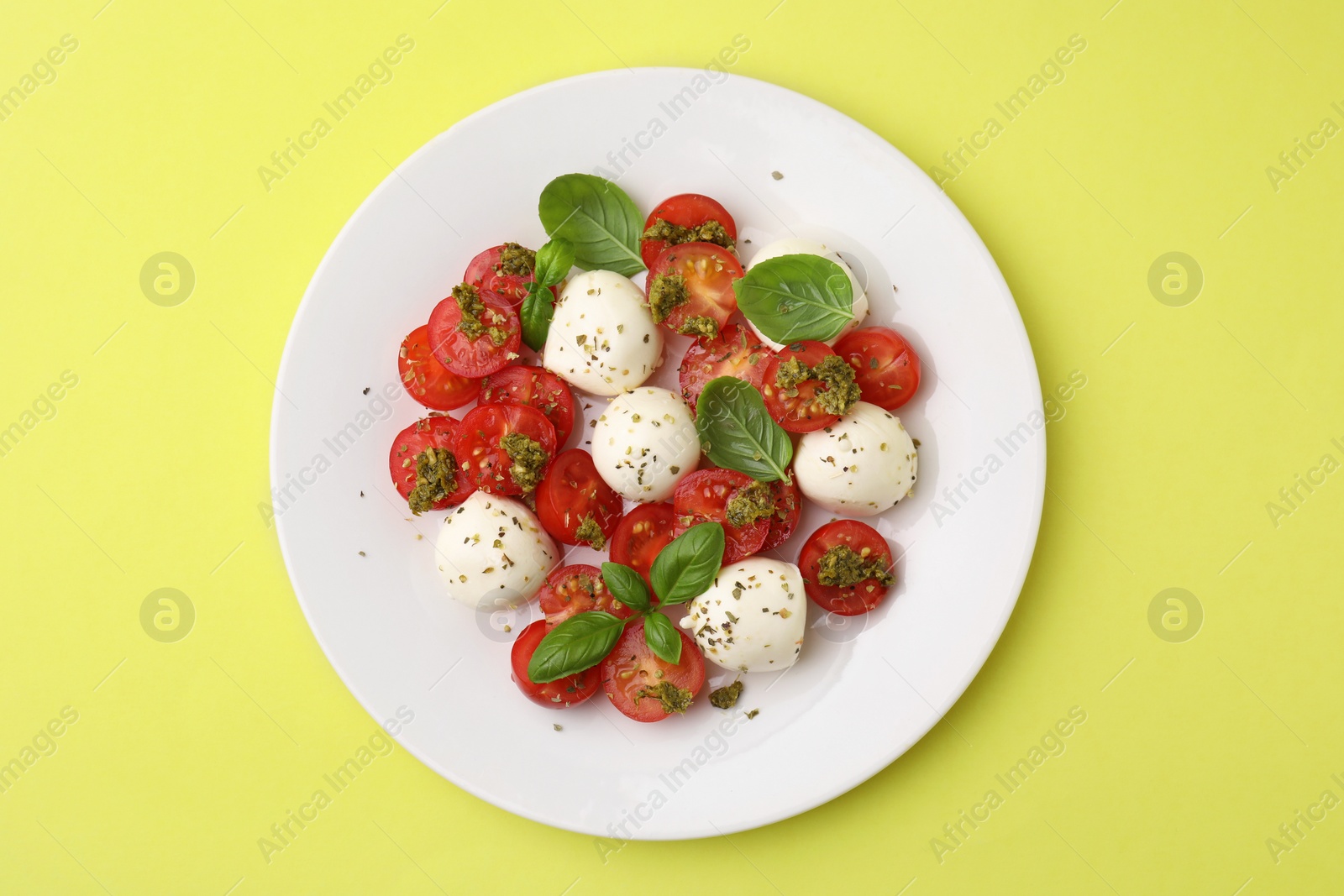 Photo of Tasty salad Caprese with tomatoes, mozzarella balls and basil on yellow background, top view