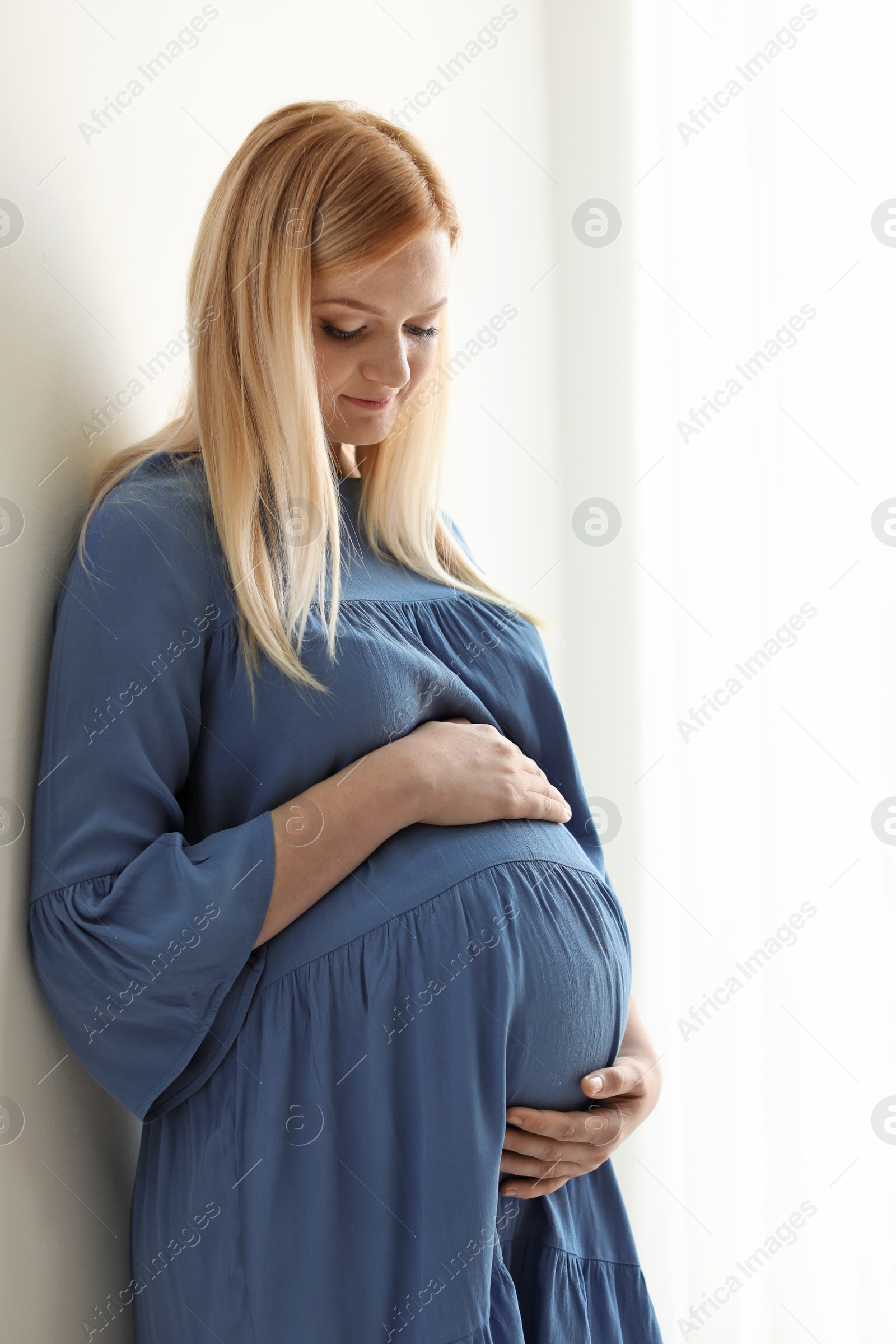 Photo of Beautiful pregnant woman near wall in light room at home