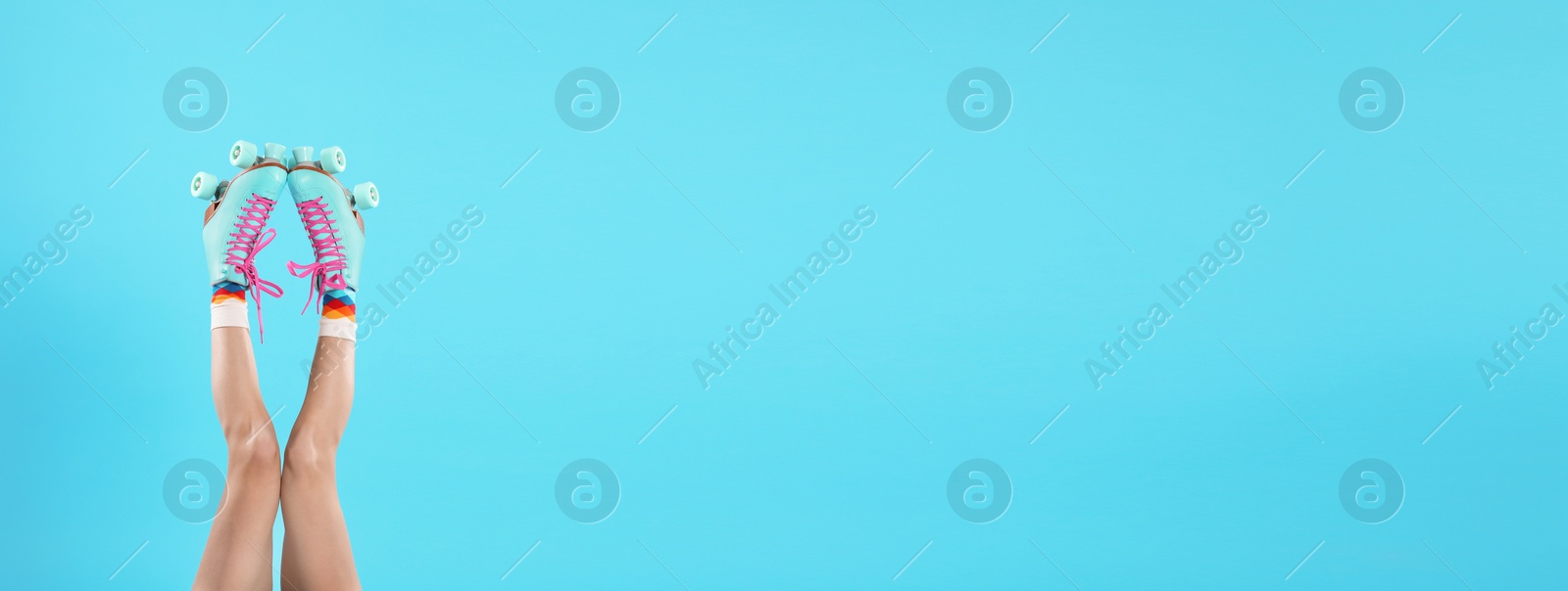 Image of Young woman with retro roller skates on light blue background, closeup. Banner design