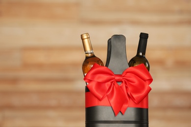 Photo of Festive package with bottles of wine against blurred background. Space for text