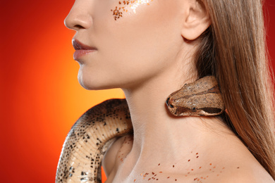Photo of Young woman with boa constrictor on bright colorful  background, closeup