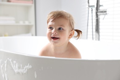 Photo of Cute little girl taking foamy bath at home