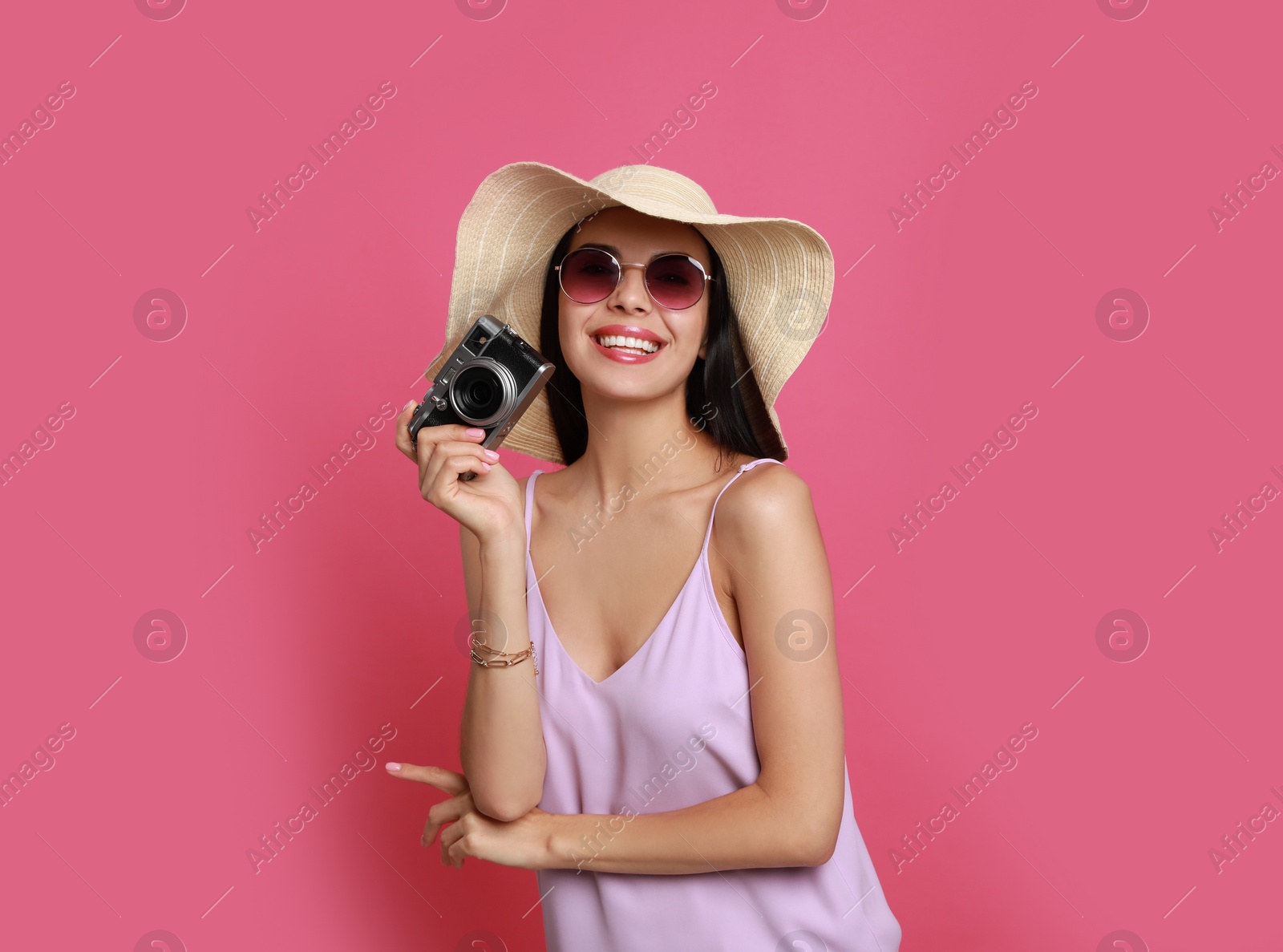 Photo of Beautiful young woman with straw hat and camera on pink background