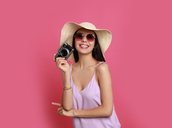 Beautiful young woman with straw hat and camera on pink background