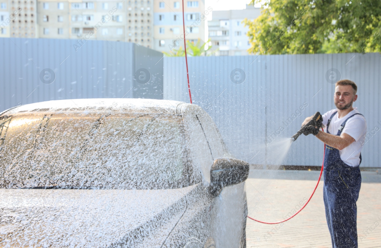 Photo of Young worker cleaning automobile with high pressure water jet at car wash