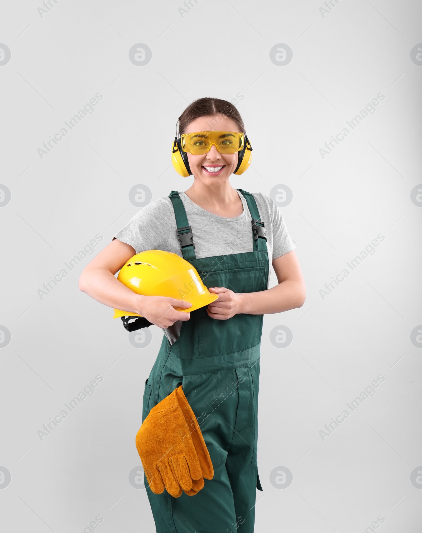 Photo of Female industrial worker in uniform on light background. Safety equipment