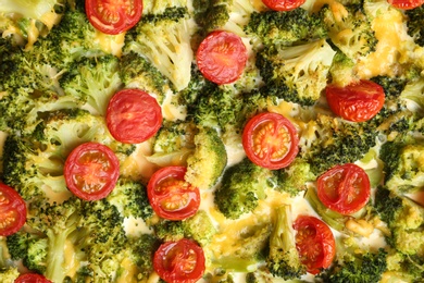 Photo of Tasty broccoli casserole with cherry tomatoes as background, closeup