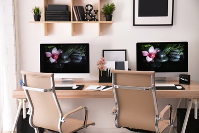 Photo of Modern workplace with large desk and computers in room. Stylish interior