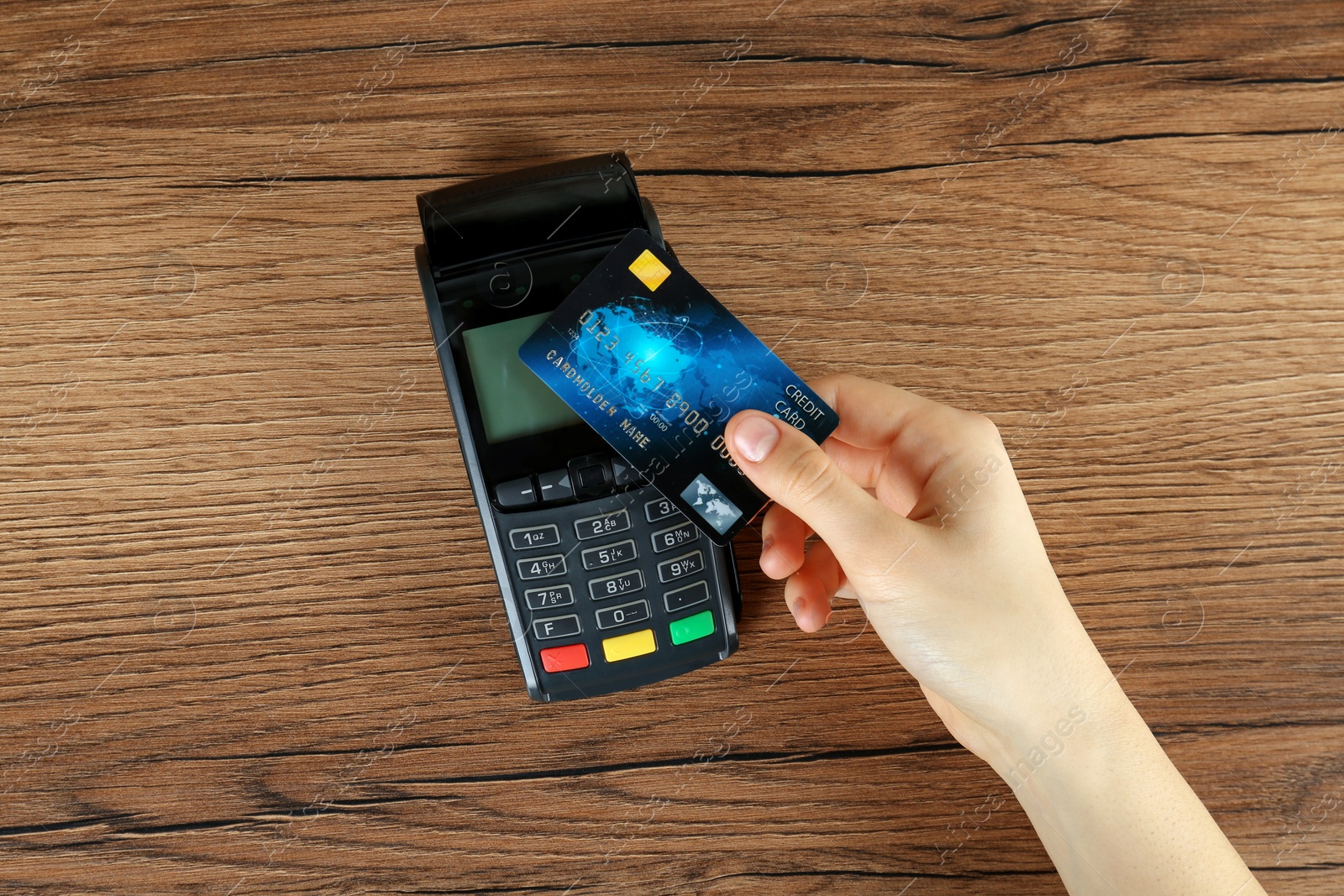 Photo of Woman with credit card using modern payment terminal at wooden table, top view