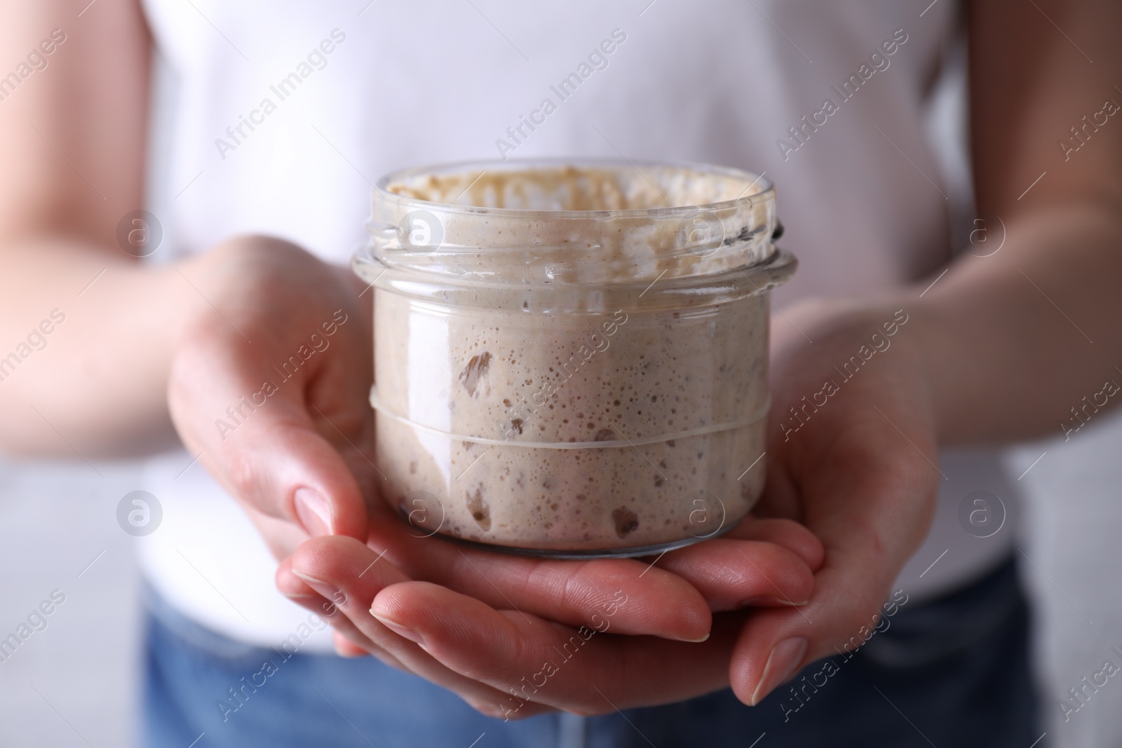 Photo of Woman holding glass jar with fresh sourdough starter, closeup