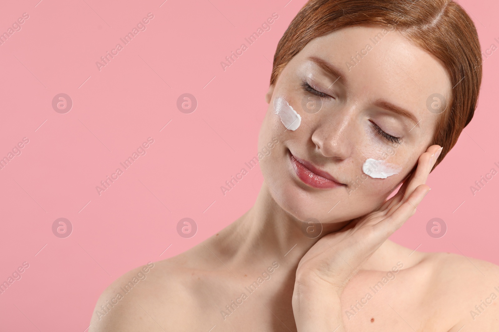 Photo of Beautiful woman with freckles and cream on her face against pink background. Space for text