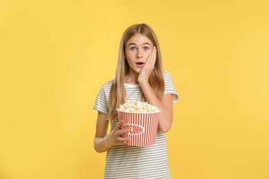 Emotional teenage girl with popcorn during cinema show on color background