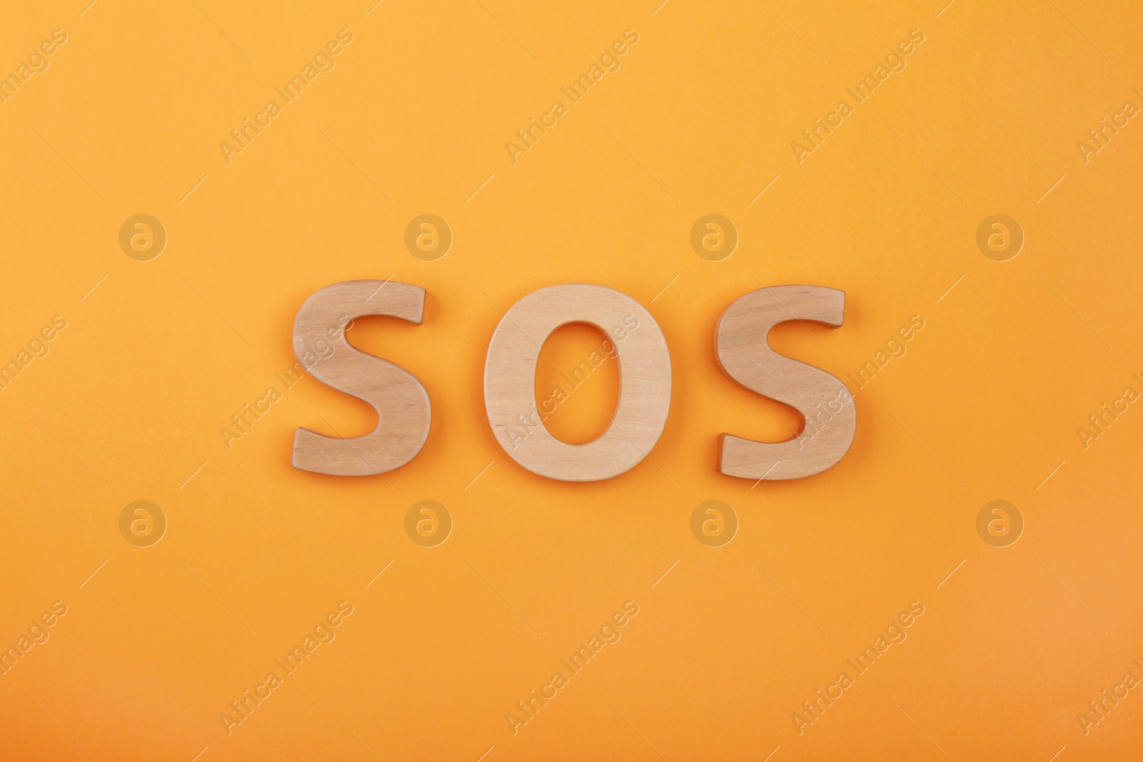 Photo of Abbreviation SOS made of wooden letters on orange background, top view