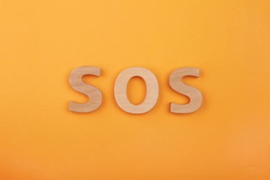 Photo of Abbreviation SOS made of wooden letters on orange background, top view