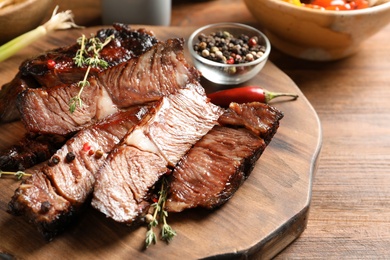 Photo of Serving board with delicious barbecued steak and spices on wooden table