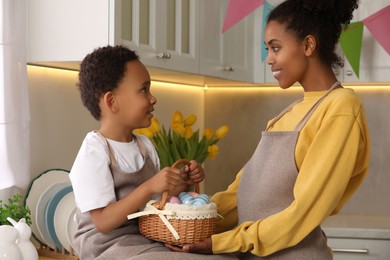 Photo of Happy African American mother and her cute son with Easter eggs in kitchen