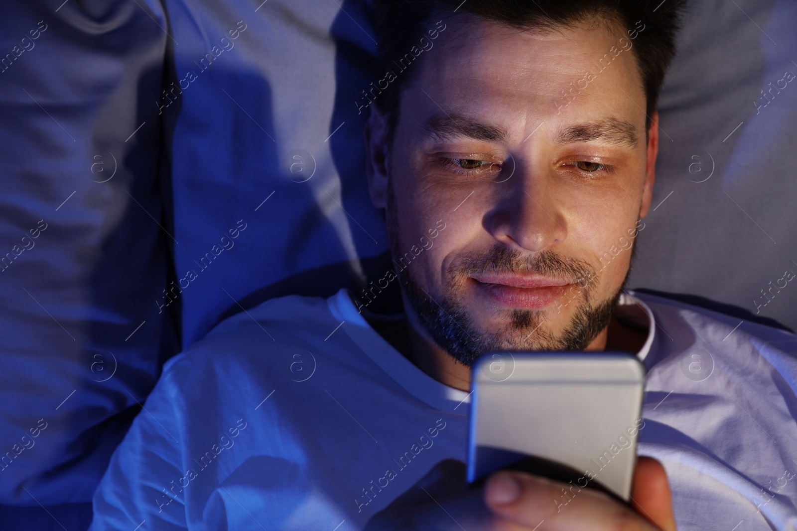Photo of Handsome man using smartphone at night, view from above. Bedtime