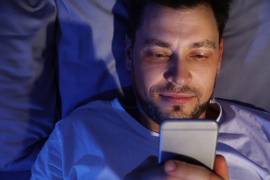 Photo of Handsome man using smartphone at night, view from above. Bedtime