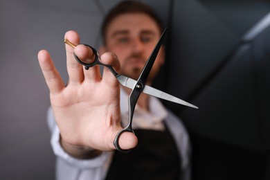 Photo of Hairdresser near dark wall, focus on professional scissors