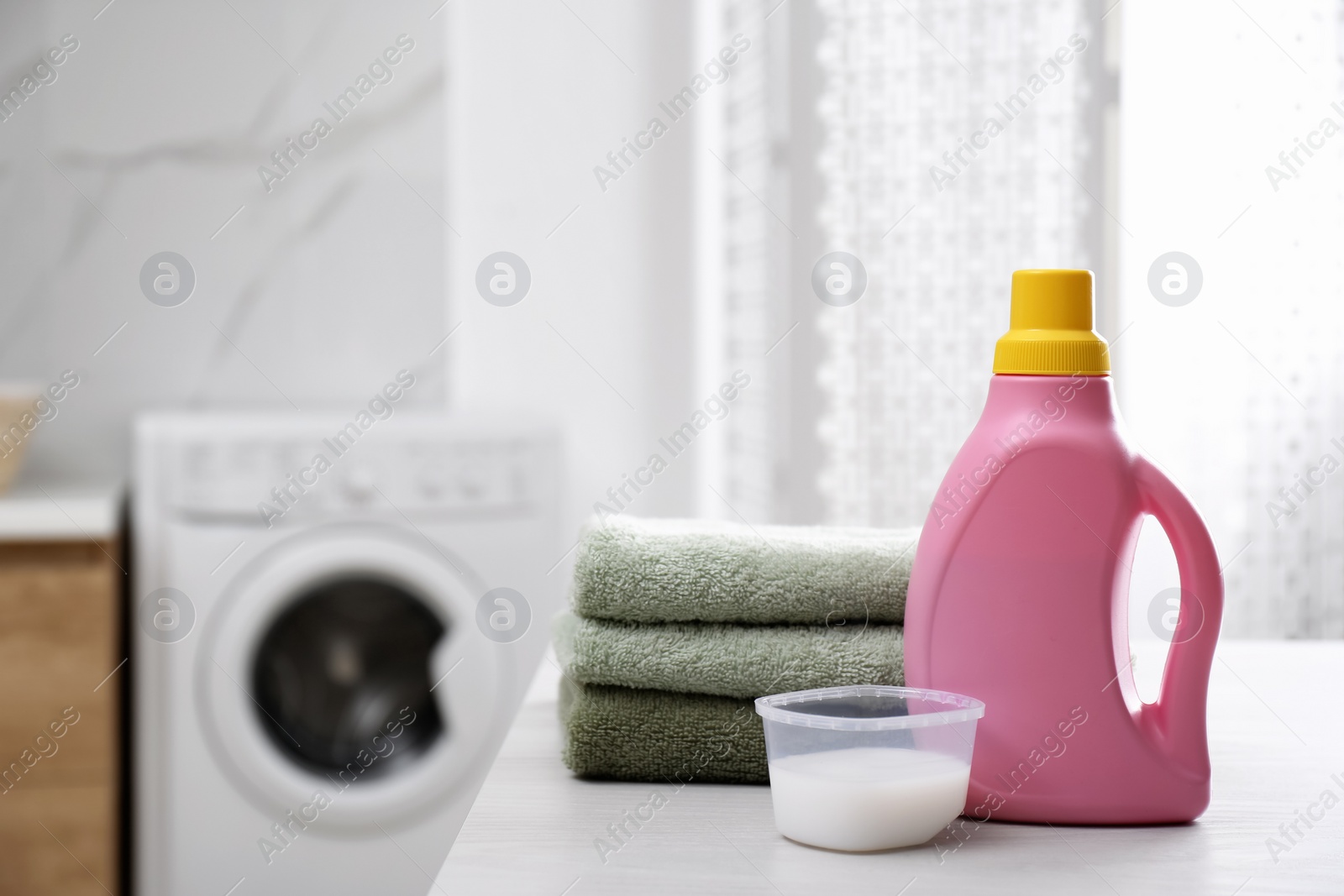 Photo of Stack of folded towels and detergents on white table in bathroom, space for text